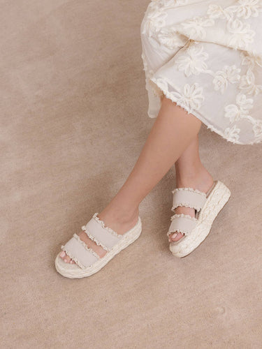 The Polly Cream Ruffle Strap Raffia Platform Slide Sandal worn with a floral dress, showcasing its playful ruffle design.