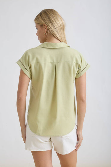 Back view of a woman wearing a COLLARED V NECK BUTTON DOWN LINE LACE DETAIL SHIRT in green with short sleeves.