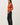 Side view of model wearing orange button-up cardigan with black pants