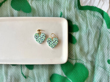 Shamrock Heart Earrings Clover Heart Earrings displayed on a plate with a green clover patterned background.