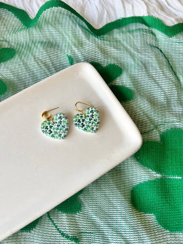 Shamrock Heart Earrings Clover Heart Earrings on a white plate against a green patterned background.