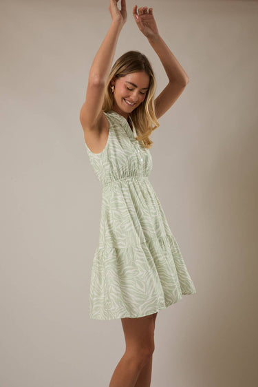 Model wearing a V NECK BUTTON UP SLEEVELESS PRINT DRESS with a playful pose in a light green print.
