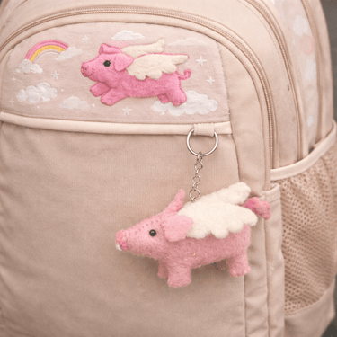 Pink felt flying pig keychain displayed on a beige pouch
