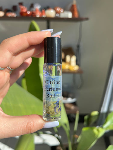 Person holding a Citrine Crystal Perfume Roller in front of a blurred background with decorative items.