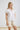 Back view of white collared V neck button down line lace detail shirt with beige shorts