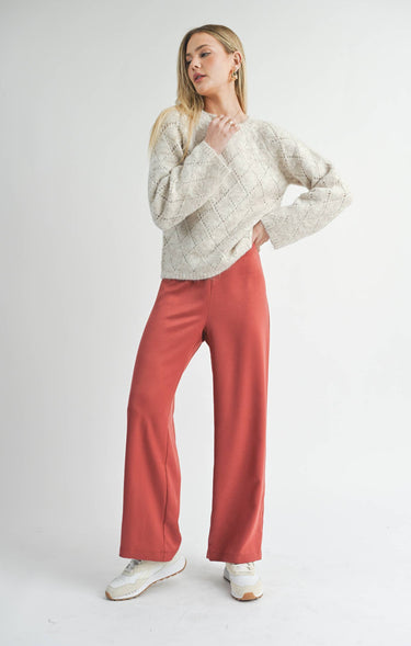 Front view of model wearing Irisha oatmeal diamond pointelle sweater with red pants