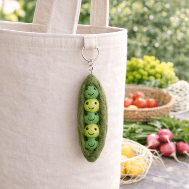 Felt Smiling Veggie Keychain - Peas in a Pod attached to a beige tote bag in a vibrant garden setting.