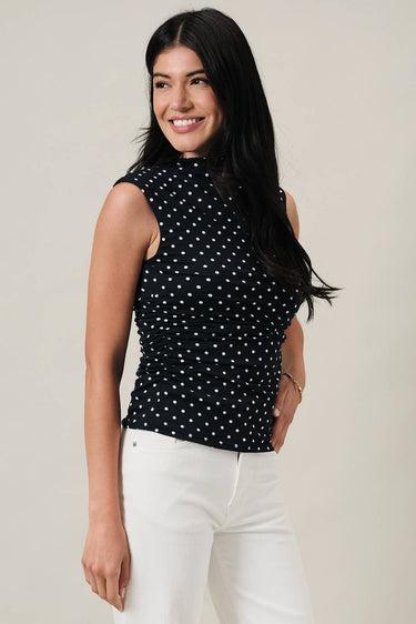 Model wearing a HIGH NECK EXTENDED SHOULDER SIDE RUCHED POLKA DOT TOP paired with white pants, showcasing a chic look.