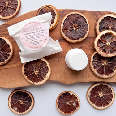 Shower Steamers - Wrapped Singles on a wooden board surrounded by dried citrus slices.