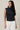 Model wearing HIGH NECK EXTENDED SHOULDER SIDE RUCHED POLKA DOT TOP with white jeans, showcasing a stylish, modern, vintage-inspired look.