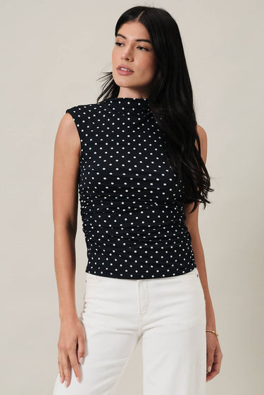 Model wearing HIGH NECK EXTENDED SHOULDER SIDE RUCHED POLKA DOT TOP with white jeans, showcasing a stylish, modern, vintage-inspired look.