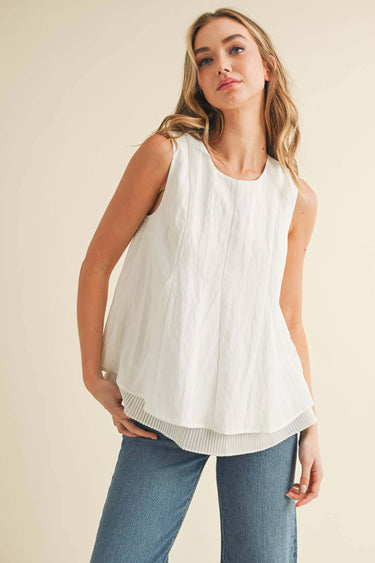 Model wearing a Pleated throughout Sleeveless A Line Top in white with layered pleating details and keyhole back.