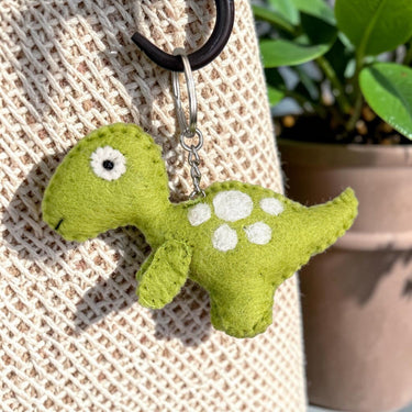 Green T-Rex dinosaur felt wool keychain hanging from a textured bag