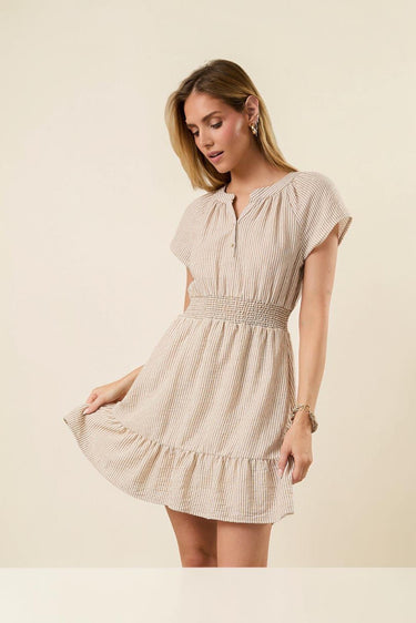 Shop Wall beige striped mini dress with notch neck, short sleeves, button-up detail, and smocked waist on a model.
