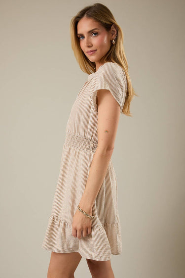 Shop Wall model wearing a beige and white striped notch neck short sleeve mini dress with a smocked waist