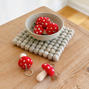 Felt Mushroom Keychain Bag Charm collection displayed in a bowl on a textured mat, showcasing their vibrant colors.