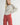 Model wearing Irisha oatmeal diamond pointelle sweater with red pants, arm extended