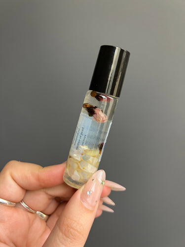 Hand holding a Mother Of Pearl Crystal Perfume Roller with floral elements in clear liquid, showcasing its elegance and design.
