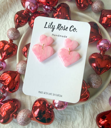 Pink Marble Heart Earrings arranged on a pink and red decorative background