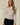 Shop Wall beige boat neck knit top with long semi-bell sleeves worn by a blonde model against a brown curtain backdrop
