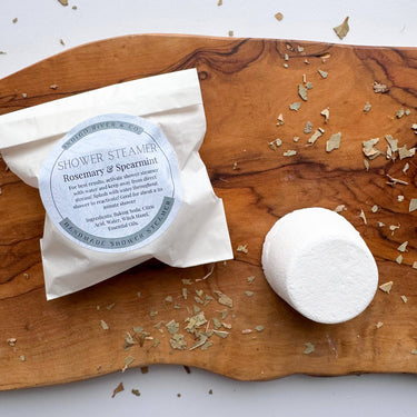 Shower Steamers -Wrapped Singles Rosemary & Spearmint scent, displayed on a wooden surface with dried herbs.