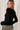 Side view of model wearing black Boat Neck Semi Bell Long Sleeve Knit Top with patterned pants