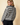 Back view of model wearing gray striped round neck long sleeve sweater with black pants