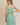 Model wearing a boat neck sleeveless side ties mini dress in green striped fabric, showcasing the back design.