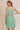 Model wearing a boat neck sleeveless side ties mini dress in green striped fabric, showcasing the back design.