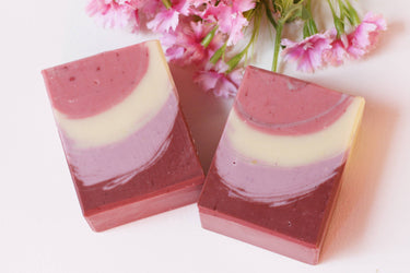 Red Feathers Organic Artisan Soap bars with floral background, showcasing natural colors and artisan design.