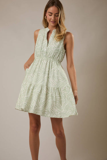 Model wearing a V NECK BUTTON UP SLEEVELESS PRINT DRESS in green with a layered skirt and pockets.