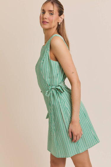 Model wearing BOAT NECK SLEEVELESS SIDE TIES MINI DRESS in green and white stripes.