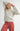 Model wearing Irisha oatmeal diamond pointelle sweater with red pants, hands raised near head
