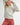 Model wearing Irisha oatmeal diamond pointelle sweater with red pants, hands raised near head