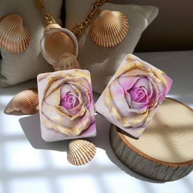 Purple Rose Gold Handmade Soap with rose design, displayed on a table with seashells and wooden slice.