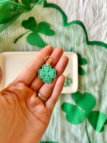 Shamrock Earrings Clover Clay Earrings Clover Earrings displayed in a hand with a green backdrop.
