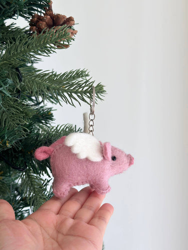 Pink felt flying pig keychain displayed with green foliage