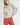 Model wearing Irisha oatmeal diamond pointelle sweater with red pants, hand on hip