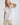 White collared V neck button down line lace detail shirt with beige shorts, seated pose