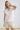 White collared V neck button down line lace detail shirt with beige shorts, seated pose
