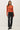 Full-length view of model wearing orange button-up cardigan with black pants