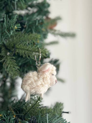 Felt Mini Sheep Keychain hanging on a green tree, handmade in Nepal from organic wool and eco-friendly dyes.