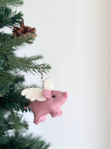 Close-up of pink felt flying pig keychain with green foliage