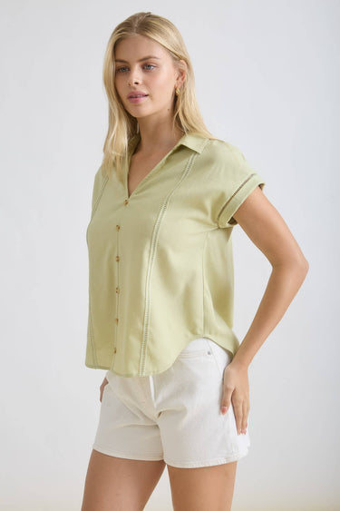 Model wearing a COLLARED V NECK BUTTON DOWN LINE LACE DETAIL SHIRT in light green, paired with white shorts.