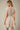 Back view of a model wearing a Shop Wall beige and white striped mini dress with short sleeves and a smocked waist.
