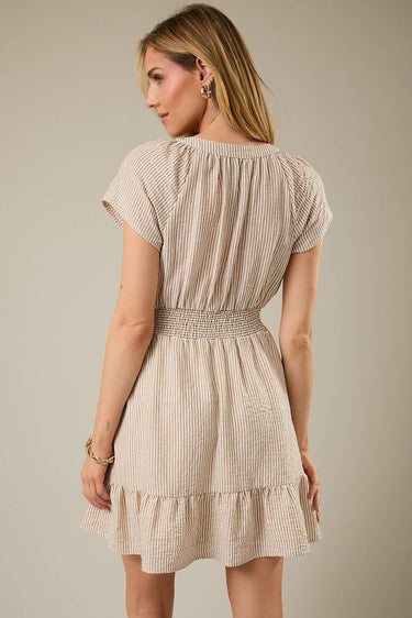 Back view of a model wearing a Shop Wall beige and white striped mini dress with short sleeves and a smocked waist.