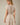 Back view of a model wearing a Shop Wall beige and white striped mini dress with short sleeves and a smocked waist.